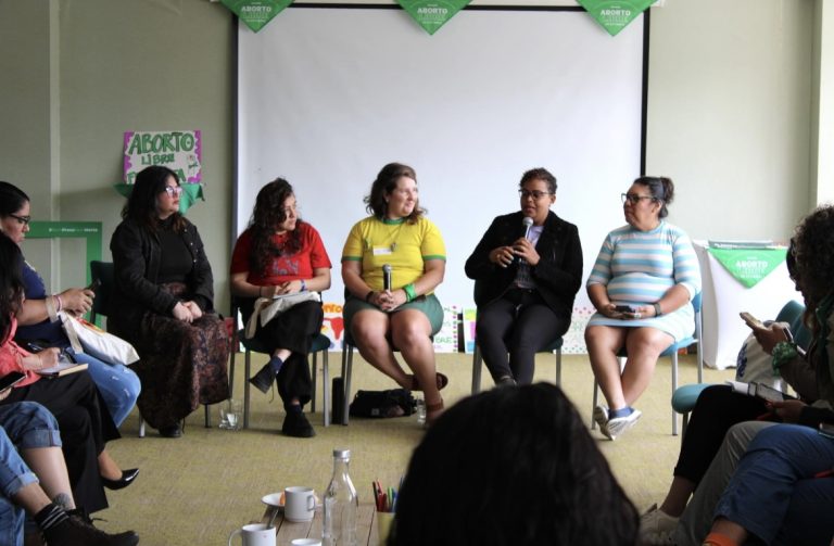 Five people are sitting in front of an audience, speaking about reproductive rights.
