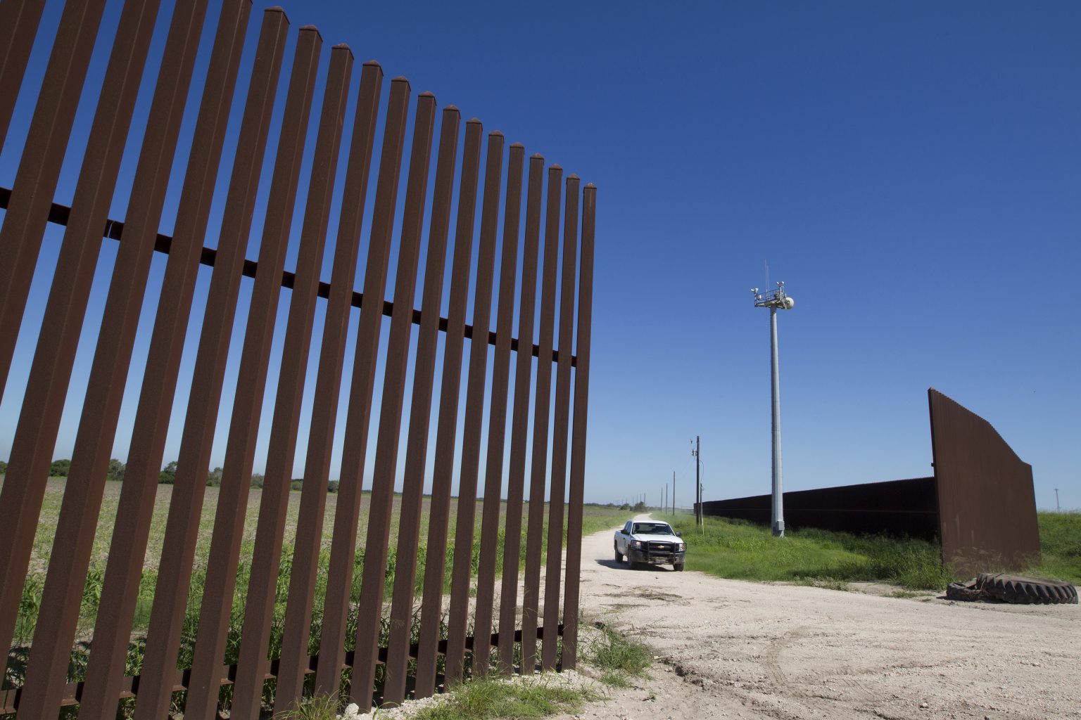 The South Texas border fence with a border patrol vehicle crossing through an entrance in the fence.