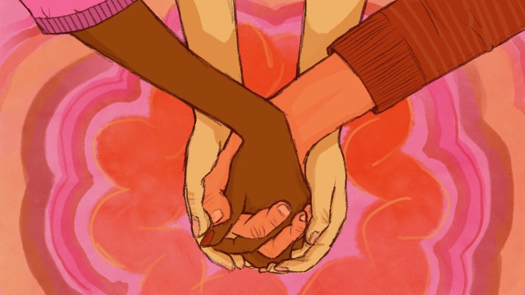 Close-up of three sets of hands; two people of different skin tones holding hands, one person’s hands in the center holding both.