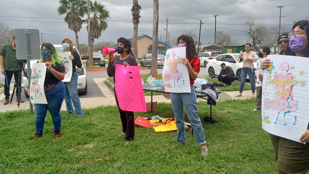 People holding posters that read “Counselors not cops” protesting outside.