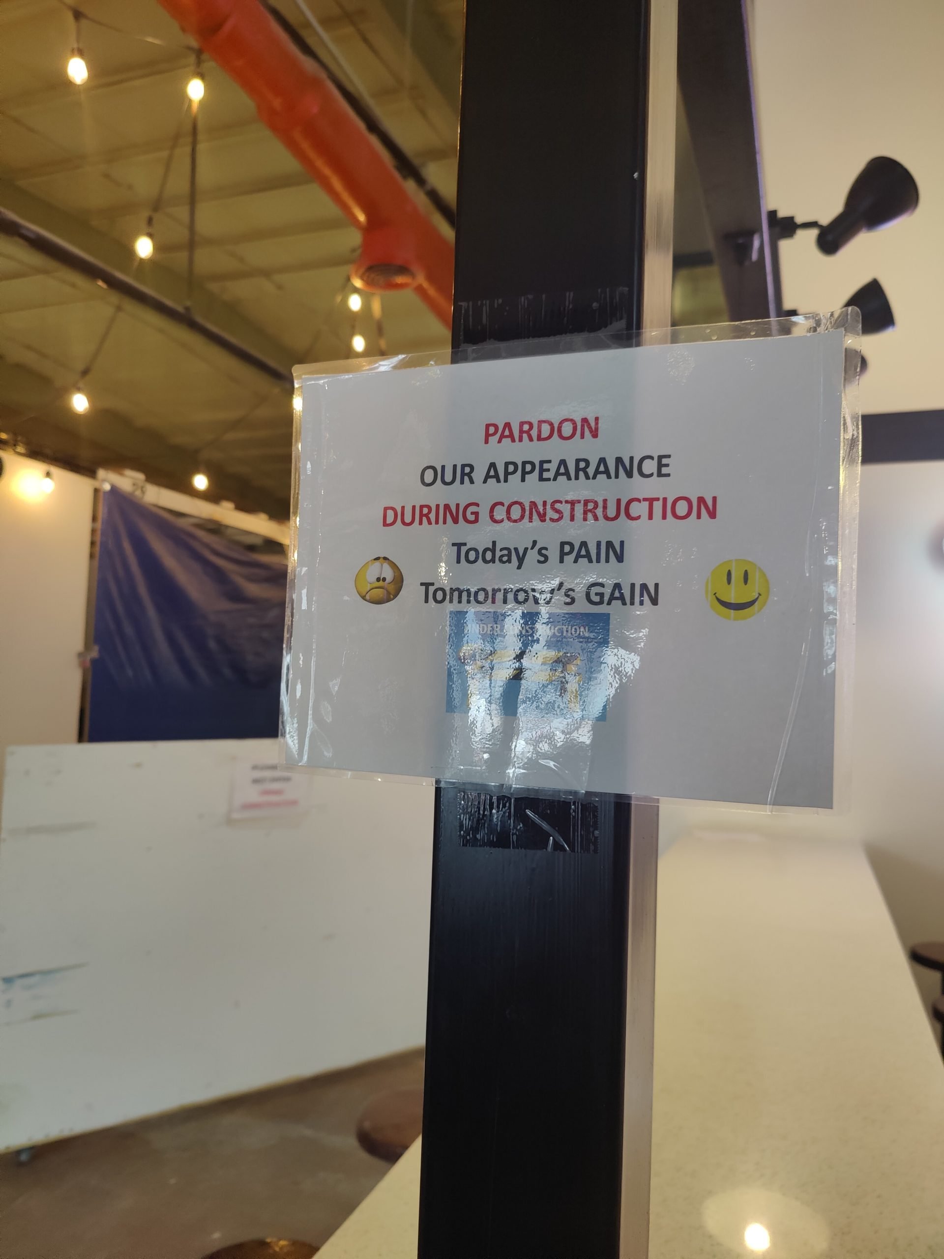 An indoor flea market currently under construction. The shops are covered by blue tarps with string lights throughout the ceiling.