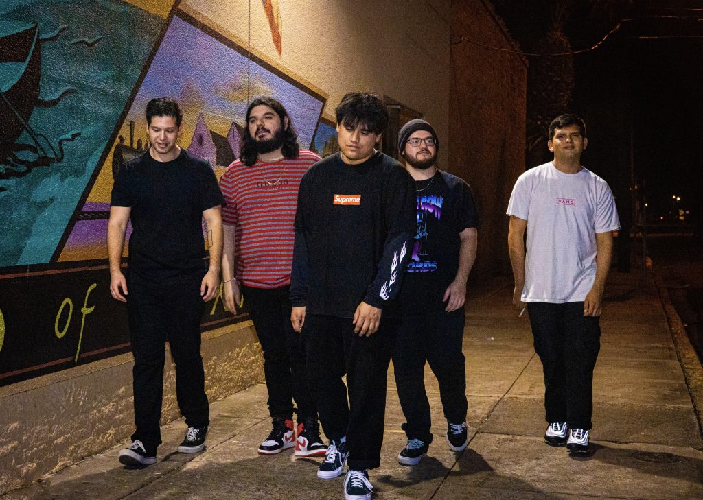 Five guys in alternative punk clothing walking and posing for a photo at a sidewalk.