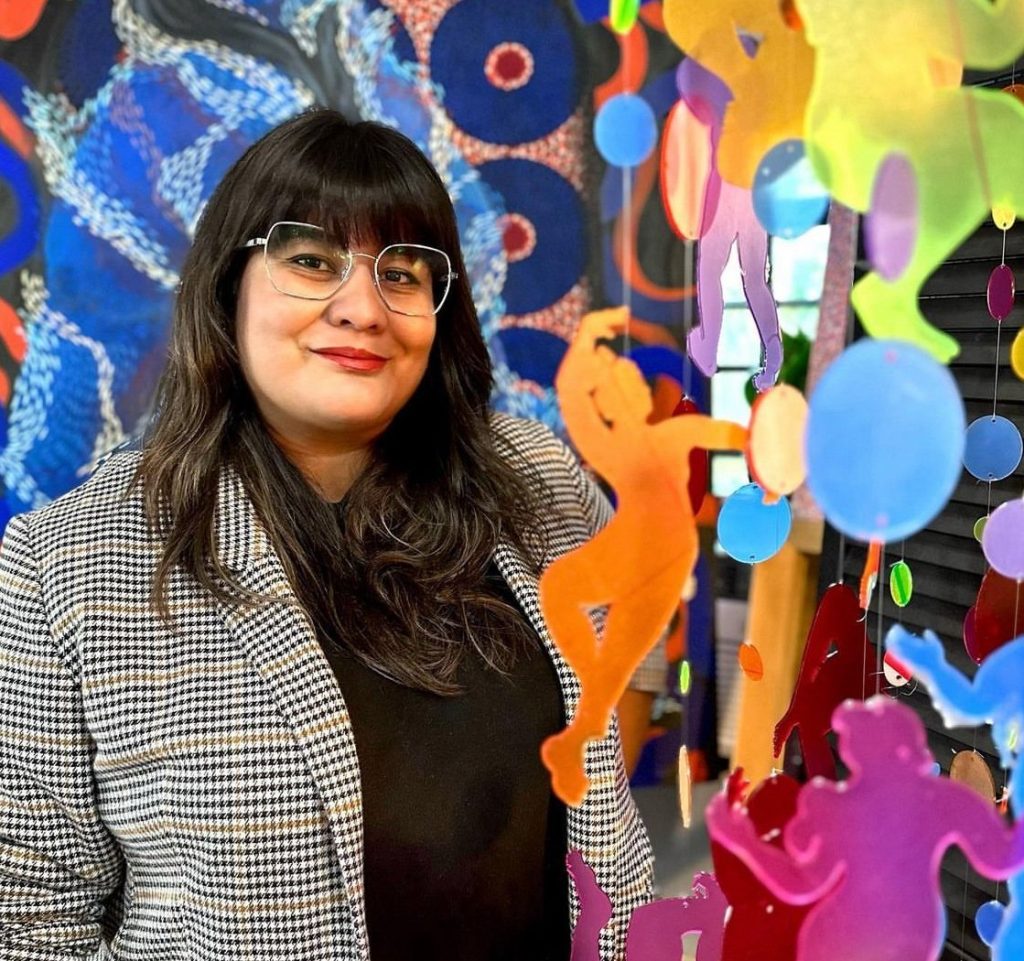 A woman standing next to her artwork, smiling at the camera.
