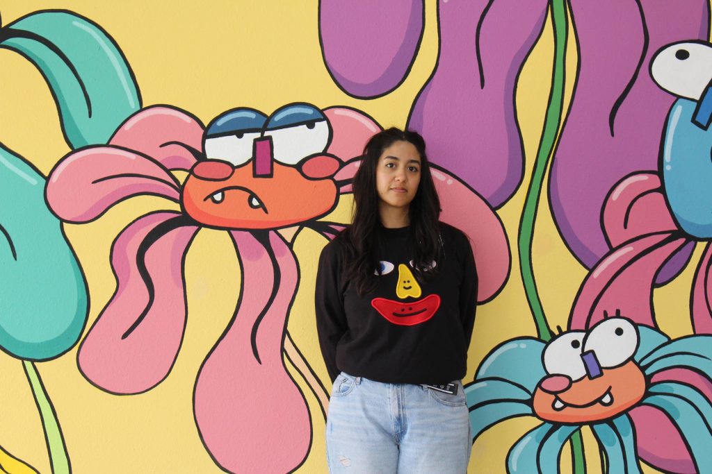 A woman in a black sweater standing in front of a colorful mural featuring cartoon characters.