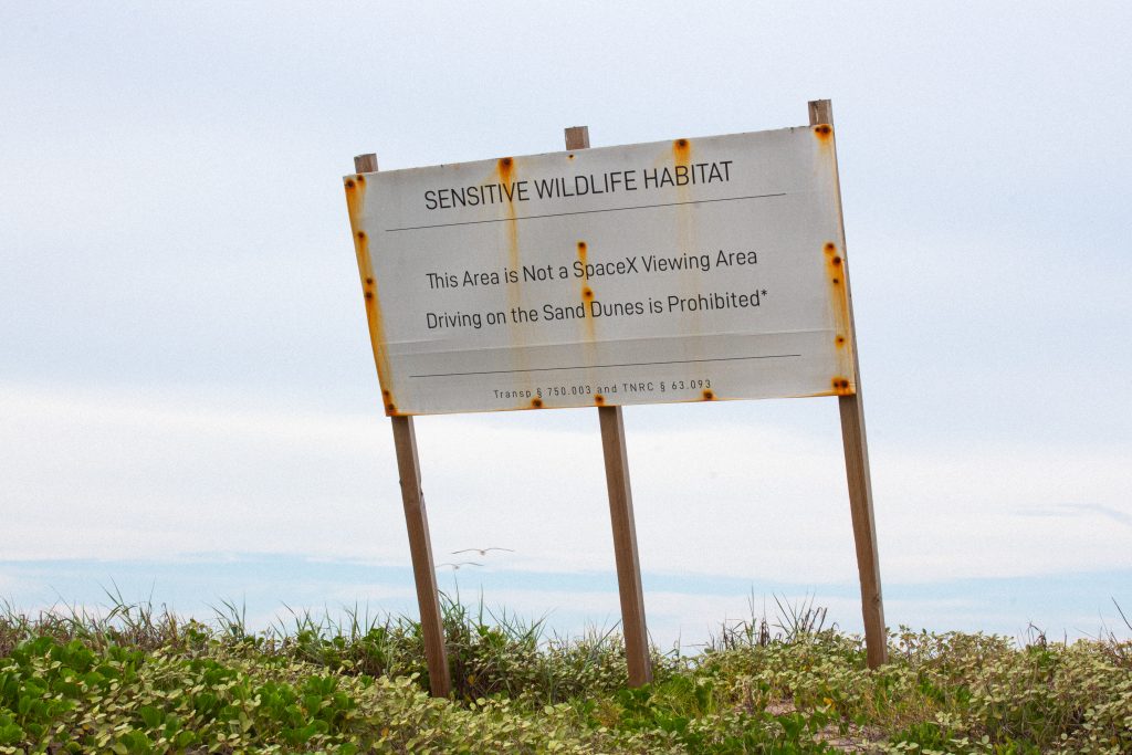 A large white sign on sand dunes meant to protect the area around Boca Chica Beach.