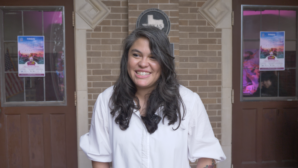 : A woman with long hair wearing a white long sleeve, smiling at the camera.