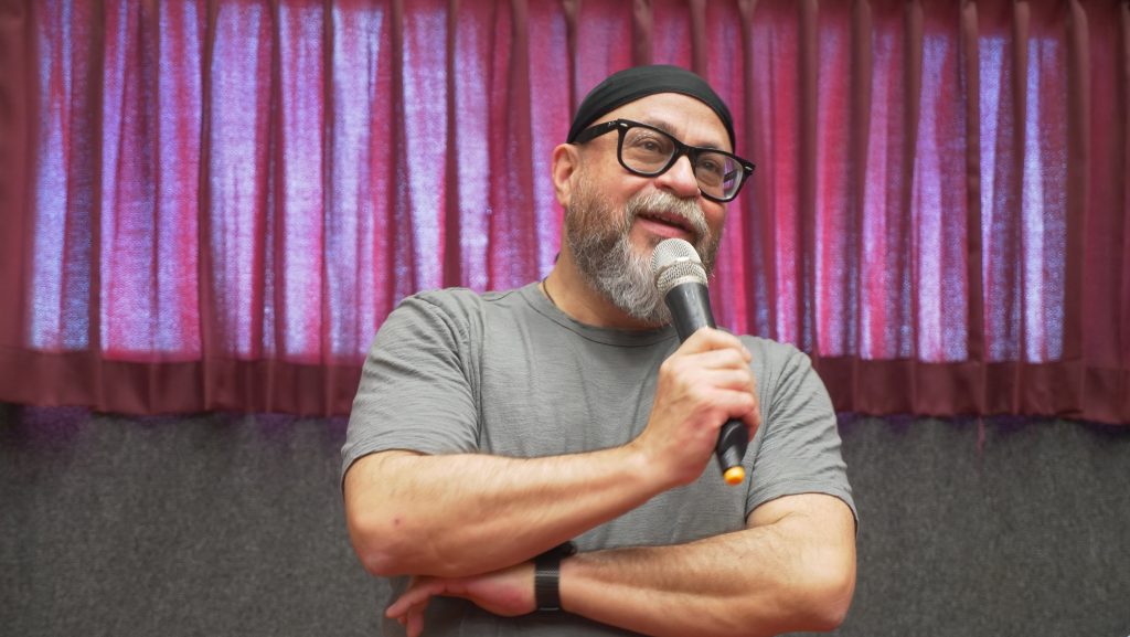 A man in a gray shirt holding a microphone.