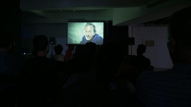 A dark room with an audience watching a film projected on a screen.
