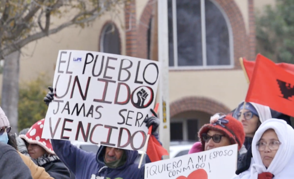 People in jackets holding up signs at a rally.