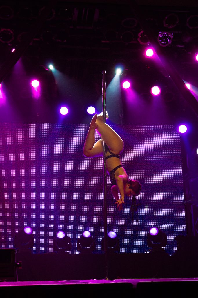 A young woman balances herself with her feet upside down on a pole.