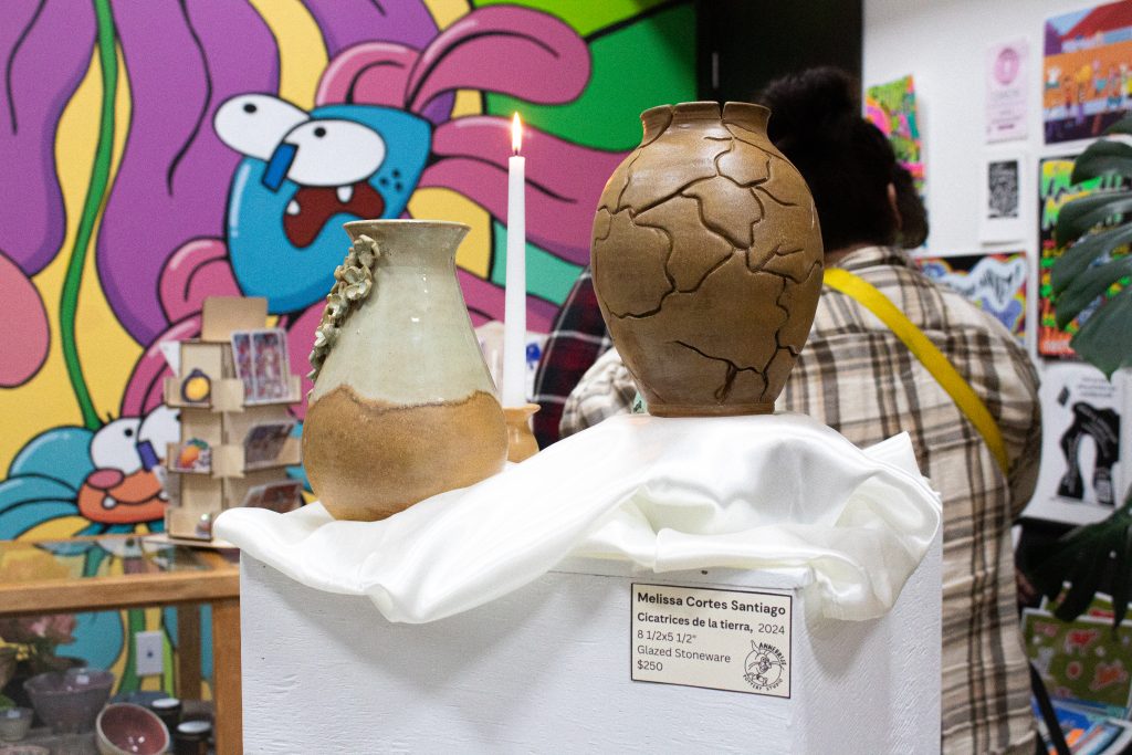 Two brown and nature-inspired colored vases are displayed on top of a piece of white fabric covering a pylon.