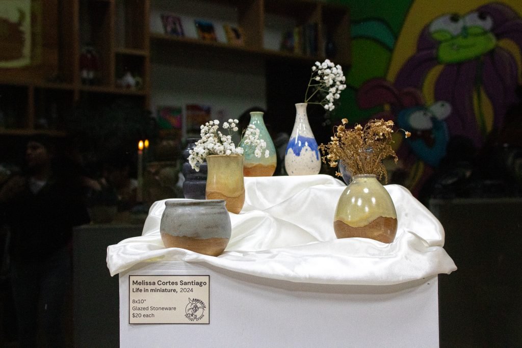 Five nature-inspired vases are displayed on top of a piece of white fabric covering a pylon, holding white flowers.