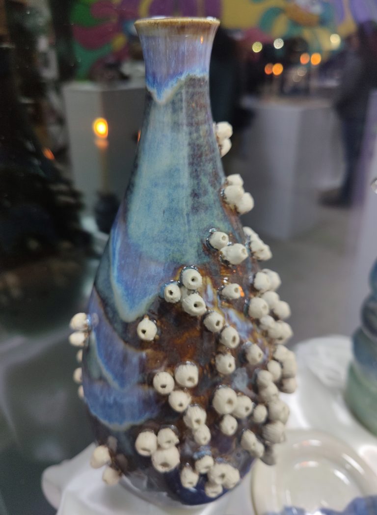 A sea green vase with ceramic barnacles all over it.