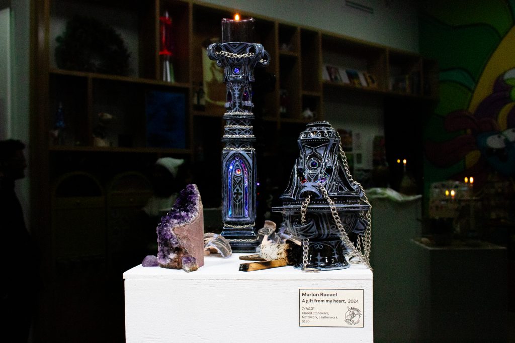 Three dark, Gothic-inspired pieces on white pylons surrounded by spiritual tools.