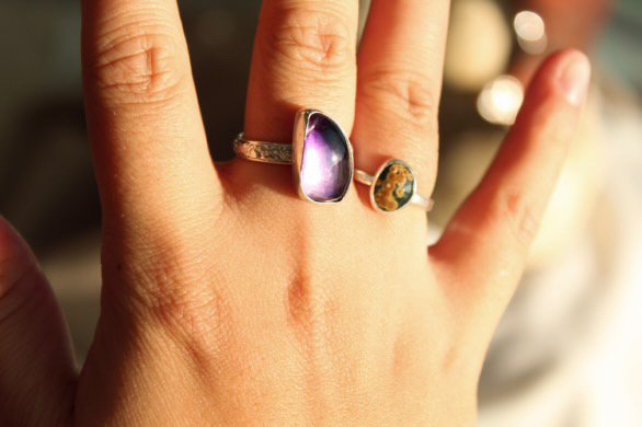 Two silver rings, one with a purple, amethyst-like stone and another with a green and yellow stone.
