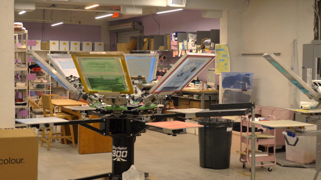 A screenprinting machine with colorful screens on it inside a warehouse.