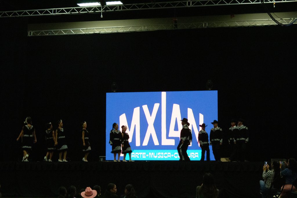 MXLAN on a projector on stage as performers gather.