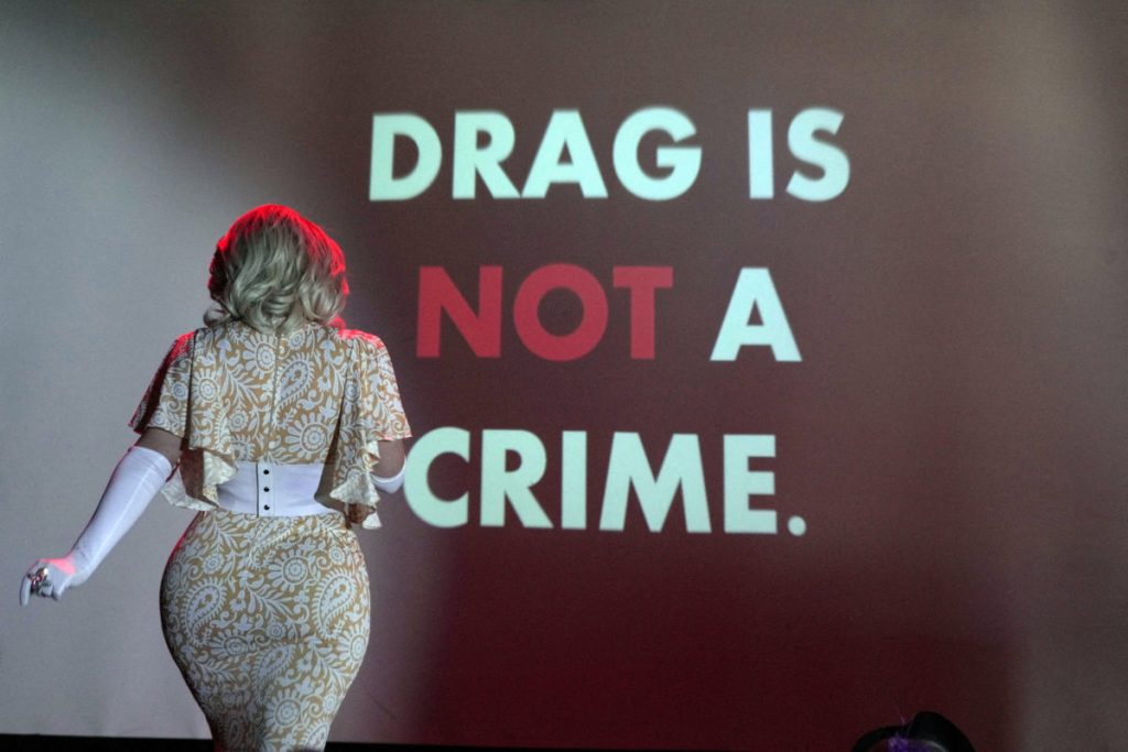 A photo of a woman’s back in front of a screen that declares, “DRAG IS NOT A CRIME.”