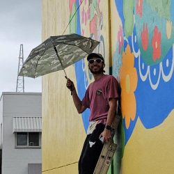 An artist in front of a yellow mural holding an umbrella in Brownsville, Texas